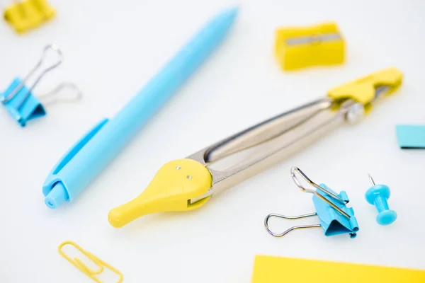 Selektiver Fokus gelb-blauer Schreibwaren mit Büroklammern, Zirkeln, Bleistiftspitzer und Stift auf weißem Hintergrund — Stockfoto