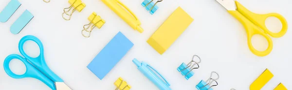 Plano panorámico de borradores amarillos y azules, bolígrafos, tijeras y clips aislados en blanco - foto de stock