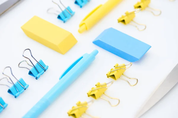 Mise au point sélective de gommes, stylos, trombones et ciseaux jaunes et bleus isolés sur blanc — Photo de stock