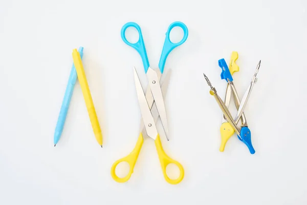 Top view of yellow and blue scissors, pens and compasses on white background — Stock Photo