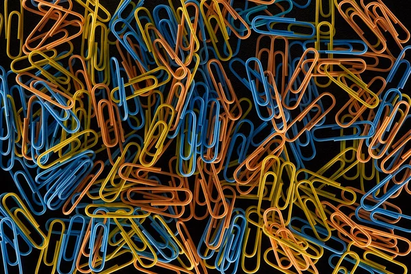 Top view of scattered yellow, orange and blue paper clips isolated on black — Stock Photo