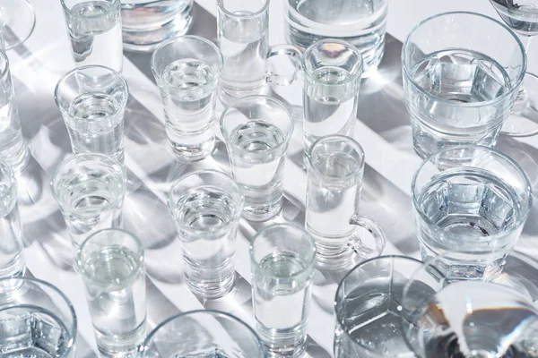 Close up view of transparent glasses with water on white background with shadows — Stock Photo