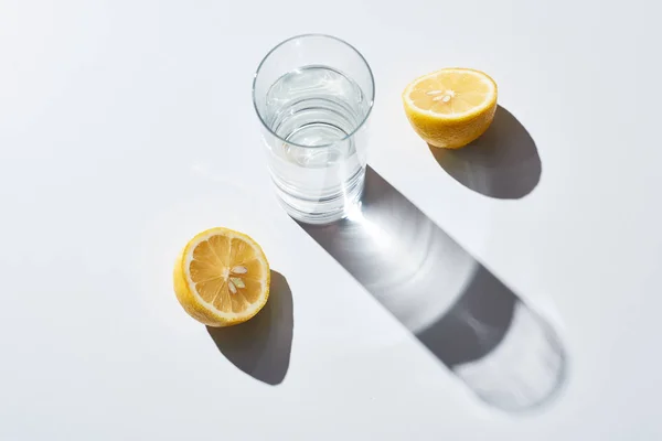 Transparent glass with water near lemon halves on white background — Stock Photo