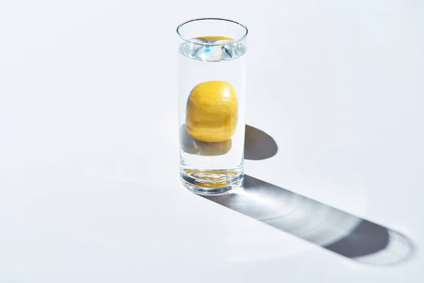 Transparent glass with water and whole lemon on white background — Stock Photo