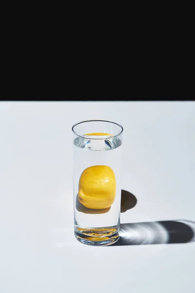 Transparentes Glas mit Wasser und ganzer Zitrone auf weißer Oberfläche isoliert auf schwarzer — Stockfoto
