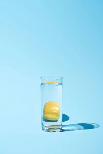 Verre transparent avec de l'eau et du citron entier sur fond bleu — Photo de stock