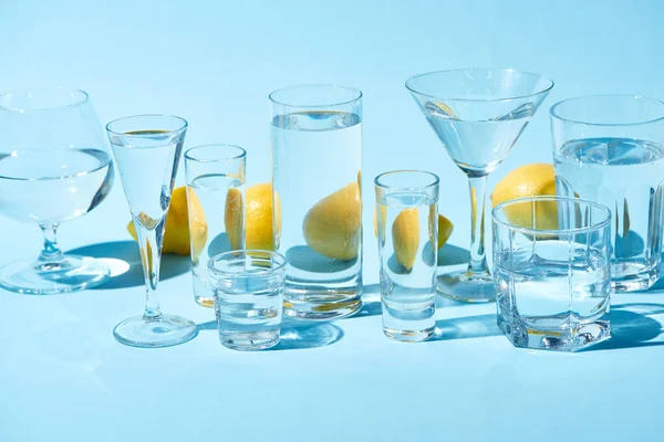 Vasos transparentes con agua y limones enteros sobre fondo azul - foto de stock