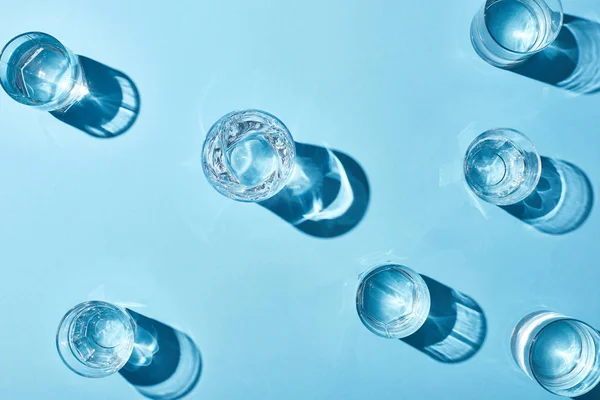 Draufsicht auf transparente Gläser mit klarem Wasser auf blauem Hintergrund — Stockfoto
