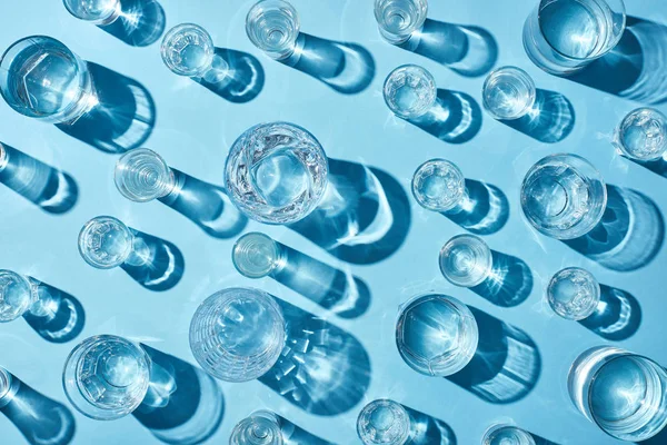 Draufsicht auf Gläser mit klarem Wasser und Schatten auf blauer Oberfläche — Stock Photo