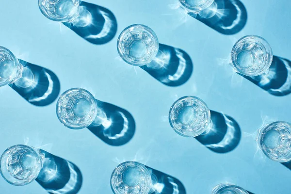 Vue de dessus des verres avec de l'eau pure et des ombres sur la surface bleue — Photo de stock