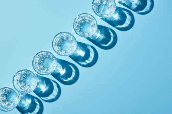 Flat lay with glasses with clear water and shadows on blue background — Stock Photo