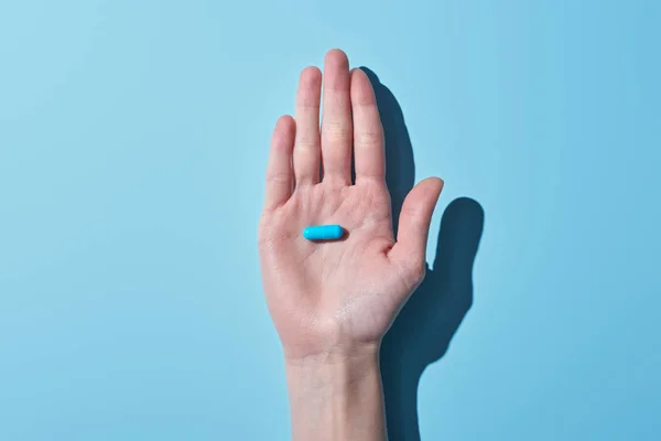 Cropped view of woman holding blue pill on palm on blue background — Stock Photo