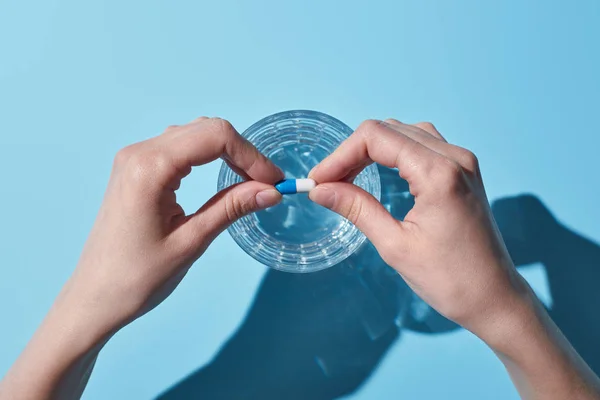 Partial view of woman putting pill in glass with water on blue background — Stock Photo