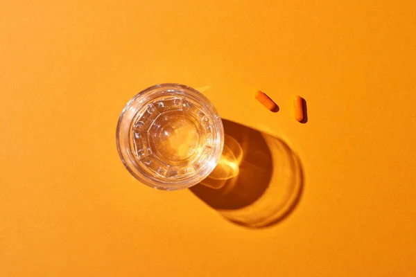 Vista superior de las píldoras cerca del vidrio con agua sobre fondo naranja — Stock Photo