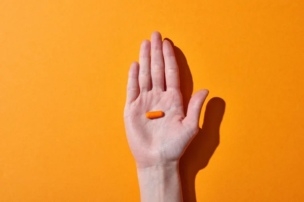 Partial view of woman holding orange pill on orange background — Stock Photo