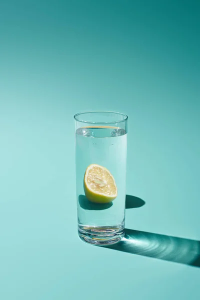 Transparent glass with fresh water and lemon on turquoise background — Stock Photo