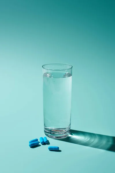 Transparent glass with fresh water and blue pills on turquoise background — Stock Photo