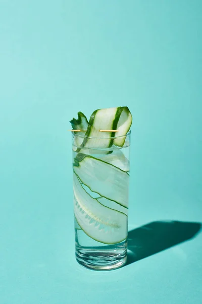 Vidrio transparente con agua dulce y rodajas de pepino sobre fondo turquesa - foto de stock
