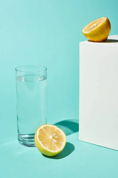 Transparent glass with pure water near lemon halves on turquoise background — Stock Photo