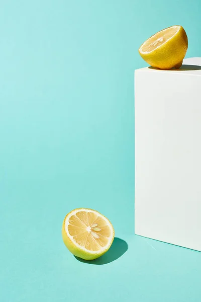 Bright lemon halves and white cube on turquoise background — Stock Photo