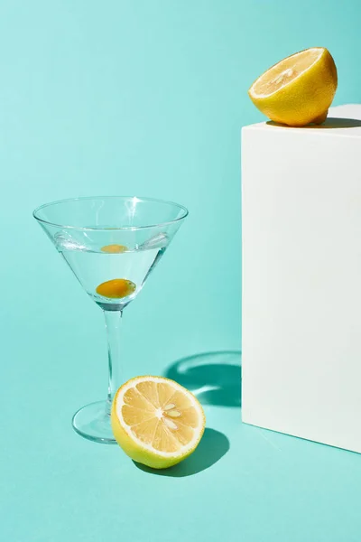 Verre transparent avec cocktail et olive près du citron sur fond turquoise — Photo de stock