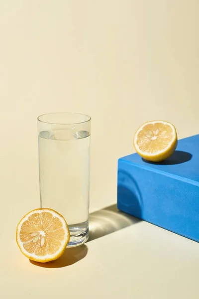 Bicchiere d'acqua vicino a metà limone e cubo blu su sfondo beige — Foto stock