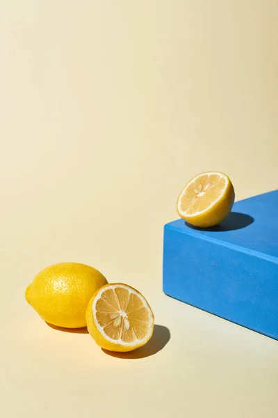 Жовті яскраві лимони біля блакитного куба на бежевому фоні — стокове фото