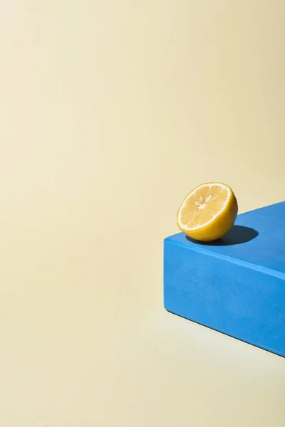 Yellow bright lemon half on blue cube on beige background — Stock Photo