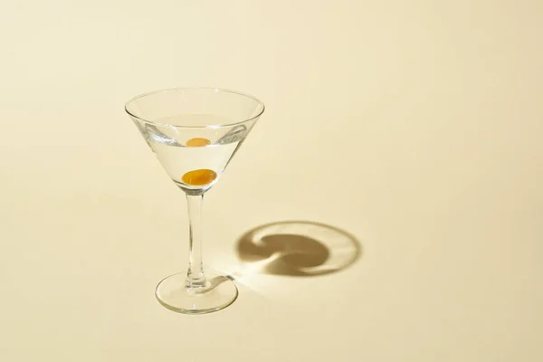 Transparentes Glas mit Cocktail und Olive auf beigem Hintergrund — Stockfoto