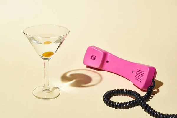 Transparent glass with cocktail and olive near pink vintage phone on beige background — Stock Photo