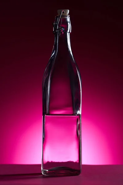 Transparente Flasche mit Wasser auf rosa Hintergrund mit Gegenlicht — Stockfoto