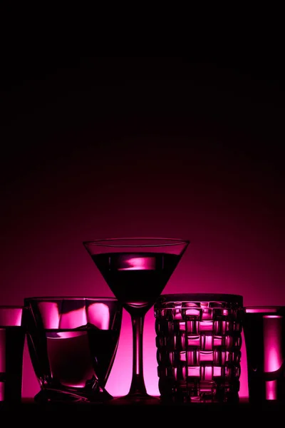 Vidros transparentes com líquido no fundo escuro com iluminação rosa — Fotografia de Stock