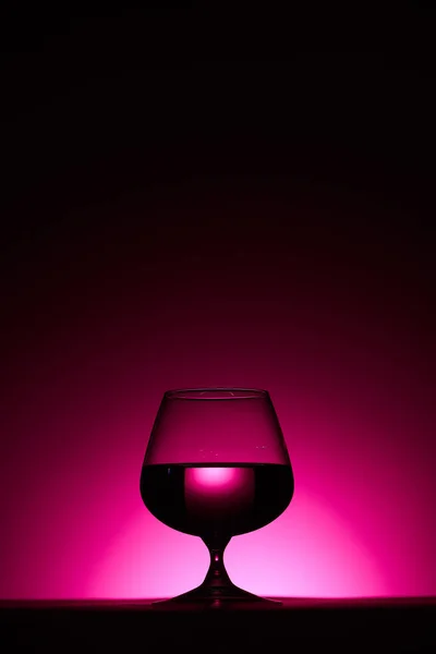 Verre transparent avec liquide sur fond sombre avec éclairage rose — Photo de stock