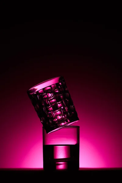 Bicchieri trasparenti con acqua su sfondo scuro con illuminazione rosa — Foto stock
