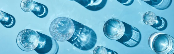 Top view of transparent glasses with clear water on blue background, panoramic shot — Stock Photo
