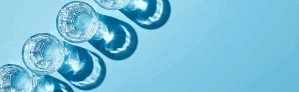 Flat lay with glasses with clear water and shadows on blue background, panoramic shot — Stock Photo