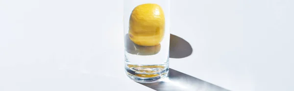Panoramic shot of transparent glass with water and whole lemon on white background — Stock Photo