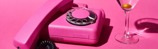 Panoramic shot of glass with cocktail and olive near vintage dial phone on pink background — Stock Photo