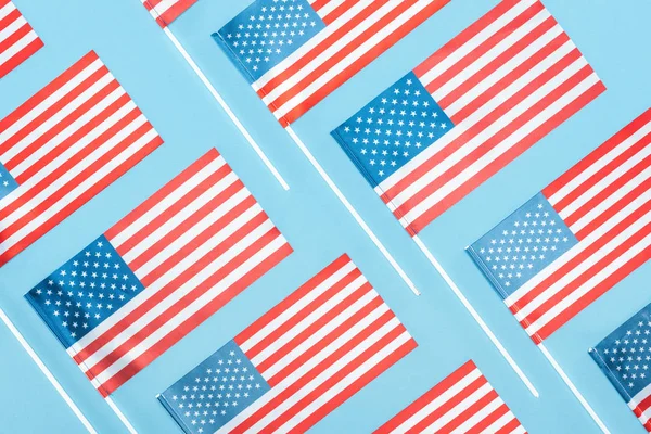 Tendido plano con banderas nacionales americanas en palos sobre fondo azul - foto de stock