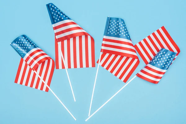 Vista superior de bandeiras americanas de cetim em paus no fundo azul — Fotografia de Stock
