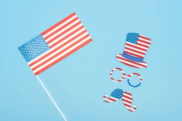 Top view of usa flag on stick near paper cut mustache, hat and glasses on blue background — Stock Photo