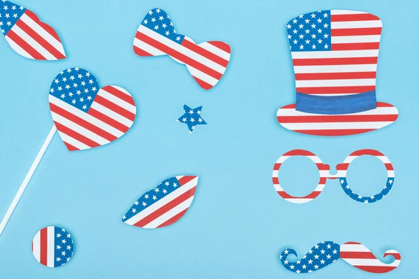 Top view of paper cut decorative mustache, glasses, hat, lips and heart made of american flags on blue background — Stock Photo