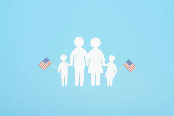 Vue du dessus de la famille de papier blanc coupé tenant des drapeaux américains décoratifs sur des bâtons de bois sur fond bleu — Photo de stock