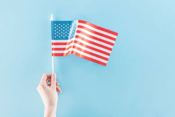 Vista parcial de la mujer sosteniendo bandera nacional americana sobre palo sobre fondo azul - foto de stock