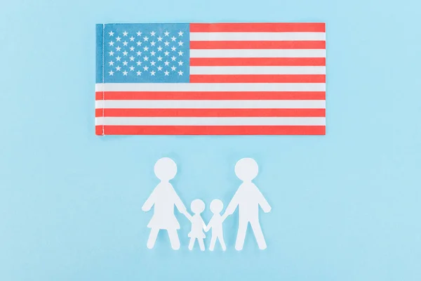 Vue du dessus du papier coupé famille blanche près du drapeau national américain sur fond bleu — Photo de stock