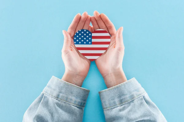 Visão parcial da mulher segurando coração feito de bandeira nacional americana em fundo azul — Fotografia de Stock