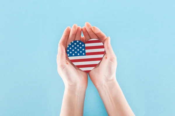 Cropped view of woman holding heart made of national american flag on blue background — Stock Photo