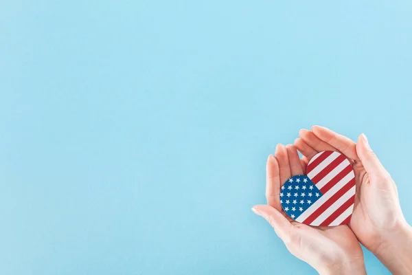 Cropped view of woman holding heart made of national american flag on blue background with copy space — Stock Photo