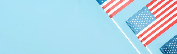 Tiro panorâmico de bandeiras americanas em paus no fundo azul com espaço de cópia — Fotografia de Stock