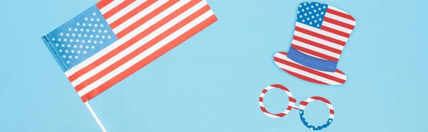 Colpo panoramico di occhiali e cappello fatto di stelle e strisce vicino alla bandiera americana su sfondo blu — Foto stock